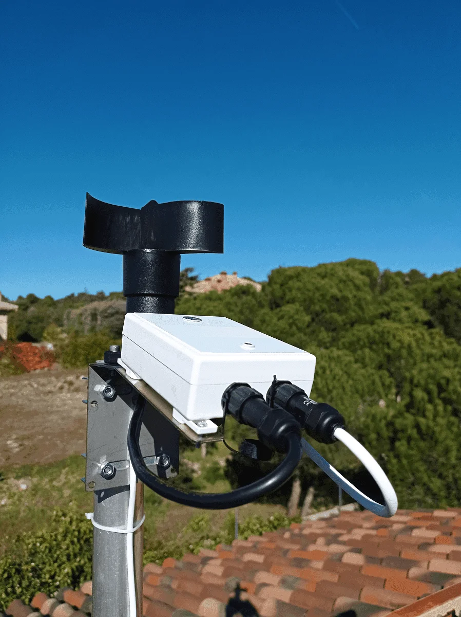 A CloudWatcher with anemometer mounted outdoors on a pole, monitoring a real sky over a Mediterranean rooftop
