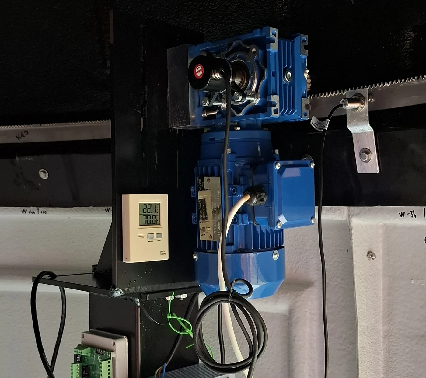 A gearmotor and worm gearbox driving the toothed rack that turns a dome, with its encoder and a thermometer on the wall beside it